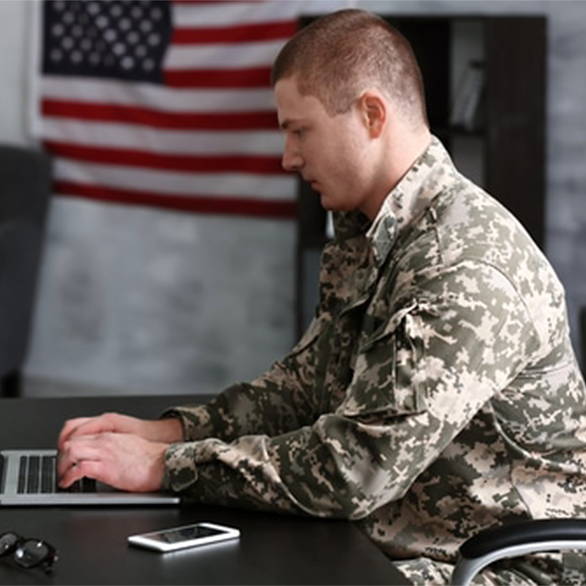 Man in a military uniform typing on a laptop